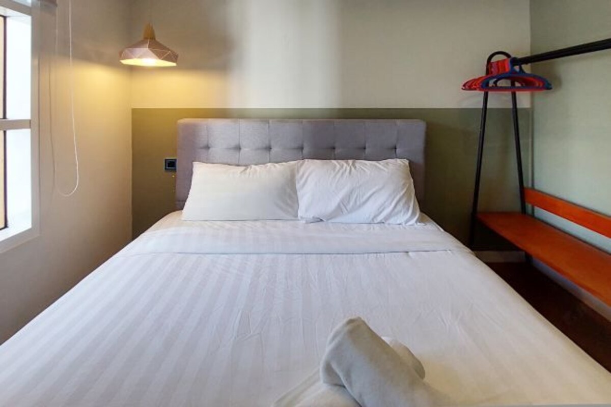 Uma cama bem arrumada com lençóis brancos, cabeceira estofada e abajur.