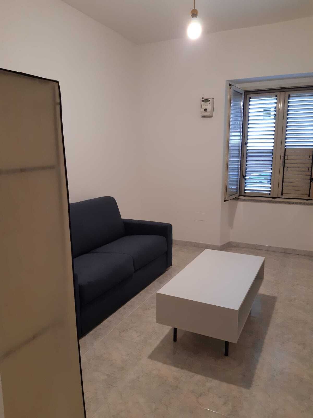 Une pièce avec un canapé de couleur sombre, une table basse blanche et une fenêtre avec des stores.