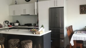 Una cocina moderna con armarios blancos, un refrigerador de acero inoxidable y una mesa de comedor de madera con mantel estampado.