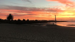 Una playa con la silueta de un faro contra un cielo al atardecer.