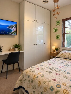 A bedroom with a bed, a desk, a chair, a wardrobe, a TV, and a window with blinds. - Elwood Seaside House (Elwood)