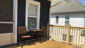 Une terrasse en bois avec une table et des chaises, une fenêtre et une rambarde.