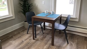 Un coin repas avec une table en bois, deux chaises, un set de table bleu et une plante en pot.