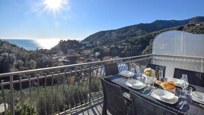 Ein Balkon mit Essbereich, mit Blick auf eine Küstenstadt und das Meer.