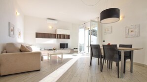 Ein modernes Wohnzimmer mit einer Couch, einem Esstisch mit Stühlen und einer Küchenzeile mit Schränken und einem Fernseher.