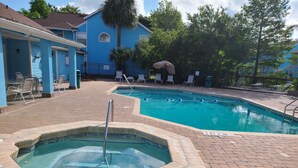 Zona de piscina con hidromasaje, sillas de descanso y un edificio azul al fondo.