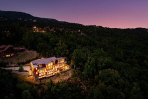 A large, multi-story building with a prominent roof, surrounded by dense forest.