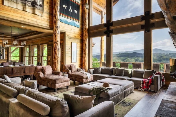 A log cabin interior with large windows, a fireplace, and a cozy seating area.