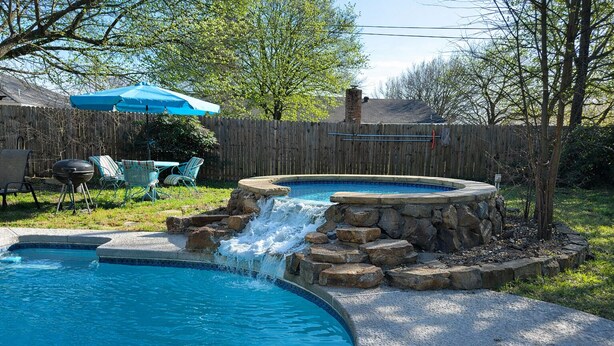 A backyard with a swimming pool, a hot tub, and a waterfall feature.