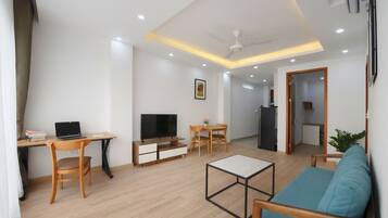 Una sala de estar moderna con sofá, mesa de centro, televisor, escritorio con ordenador portátil y zona de comedor.