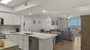 Une cuisine moderne avec des meubles blancs, un îlot central et un coin repas avec des chaises bleues.
