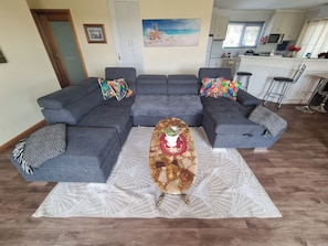 Un salon moderne avec un canapé d’angle gris, une table basse dotée d’un plateau décoratif et un tapis à motifs.