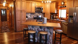 A wooden cabin-style kitchen with a central island, stone backsplash, and wooden cabinets. - Peaceful Pines (Custer)