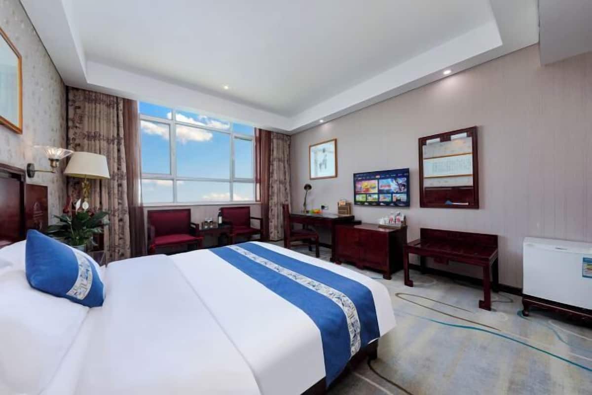 Une chambre d’hôtel avec un grand lit, un bureau, une chaise, une petite table et une fenêtre donnant sur un beau paysage.