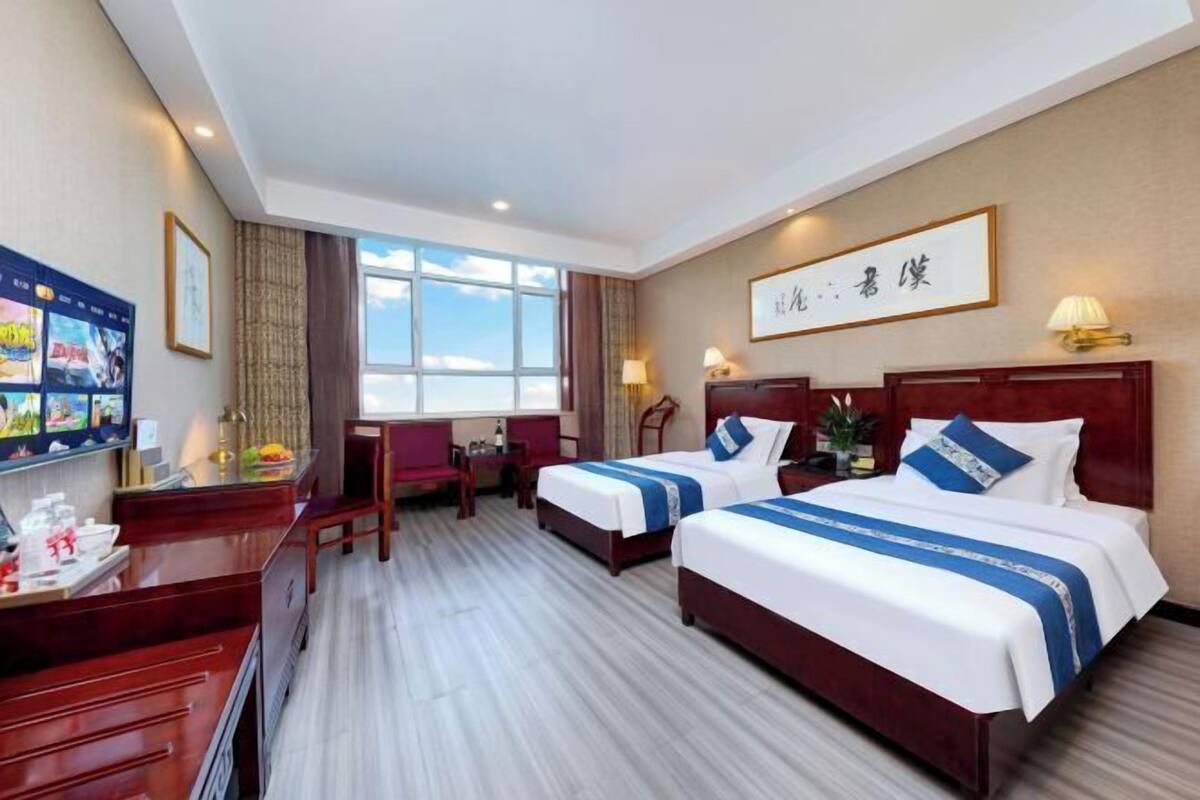 Une chambre d’hôtel avec deux lits, un bureau, une chaise, une télévision et une grande fenêtre.