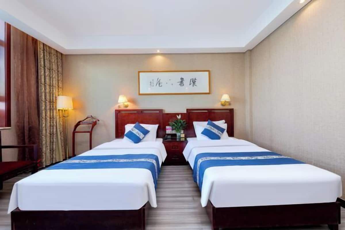 Une chambre d’hôtel avec deux lits, une table de chevet, une lampe et une œuvre d’art encadrée au mur.