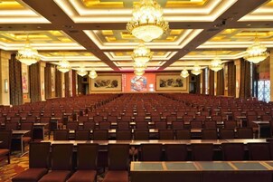 Un salón de conferencias con filas de sillas, un escenario y una araña de cristal.