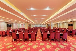 Un salón de conferencias amplio con filas de mesas y sillas, una alfombra roja y un techo alto con iluminación empotrada.