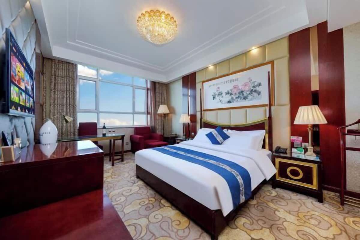 Une chambre d’hôtel avec un grand lit, un bureau, une chaise, une lampe de bureau, une table de chevet et une fenêtre.