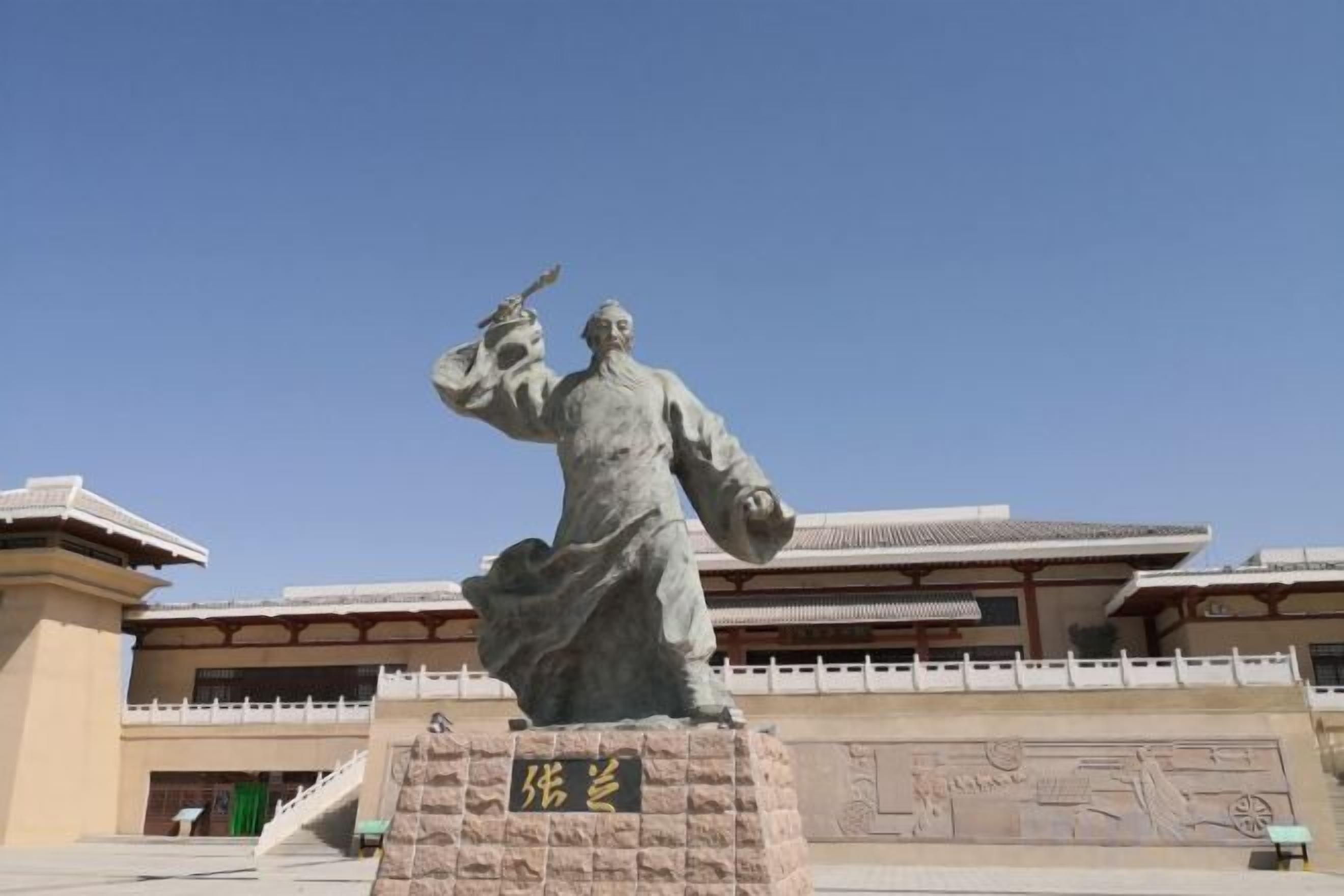 Une statue se dresse devant un bâtiment traditionnel, sous un ciel dégagé.