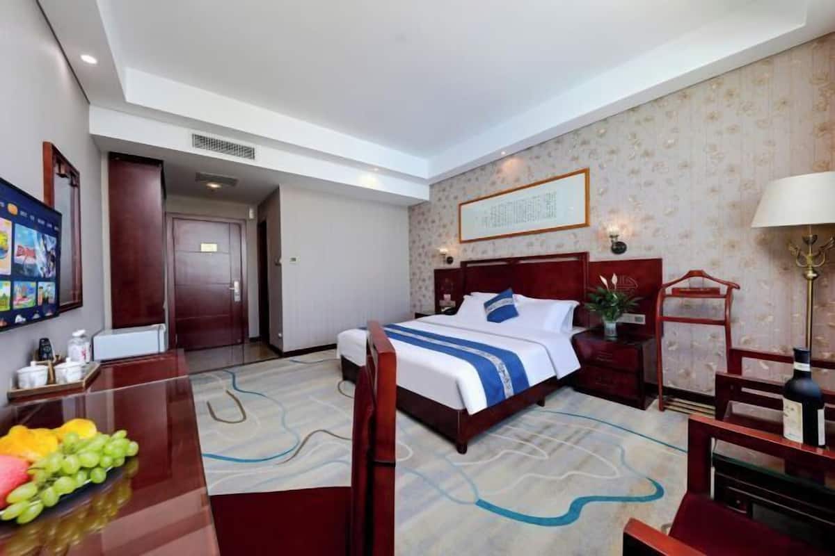 Une chambre d’hôtel avec un grand lit, un bureau agrémenté d’un panier de fruits, une chaise, une table de chevet et une œuvre d’art accrochée au mur.