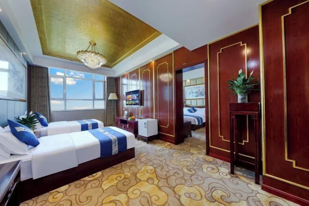 Une chambre d’hôtel avec deux lits, un lustre, une grande fenêtre et un panneau décoratif au mur.