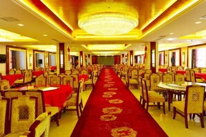 Une salle de banquet avec des rangées de tables et de chaises, un tapis rouge et un lustre.