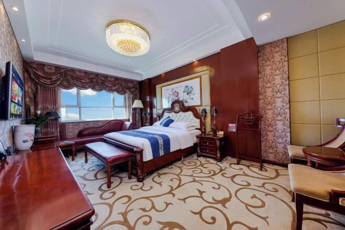 Une chambre d’hôtel avec un grand lit, un bureau, une chaise, une table de chevet et un lustre.
