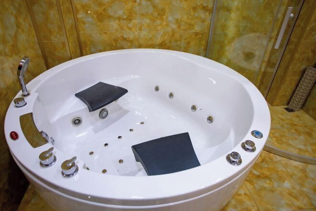 Une baignoire blanche dotée de plusieurs jets et d’un pommeau de douche à main, le tout installé devant un mur de marbre.