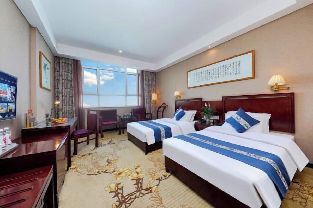 Une chambre d’hôtel avec deux lits, un bureau, une chaise et une grande fenêtre.