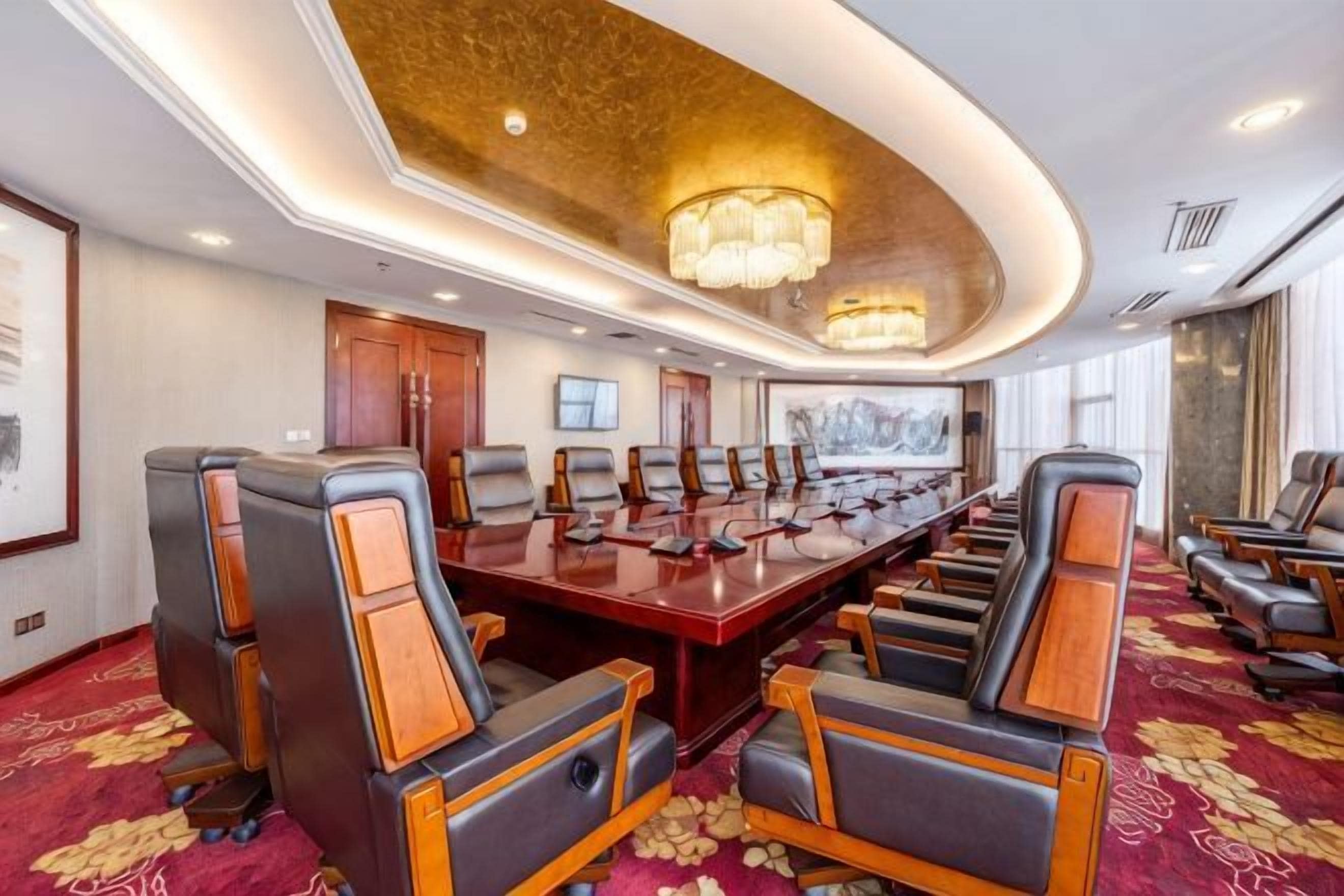 Un salón de conferencias con una larga mesa y múltiples sillas, un candelabro y suelo alfombrado.