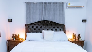 Een netjes opgemaakt bed met een gestuufd hoofdbord, twee nachtkastjes met lampen, en een grijze gordijn.