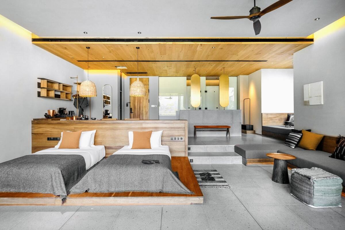Una habitación de hotel moderna con techo de madera, dos camas, un sofá, una mesita y un banco.