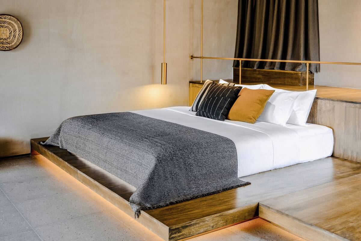 Un dormitorio moderno con una cama plataforma de madera, ropa de cama blanca y un plaid estampado.