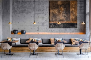 Un interior moderno con una zona de estar con banca de madera, sillas de metal e iluminación colgante.