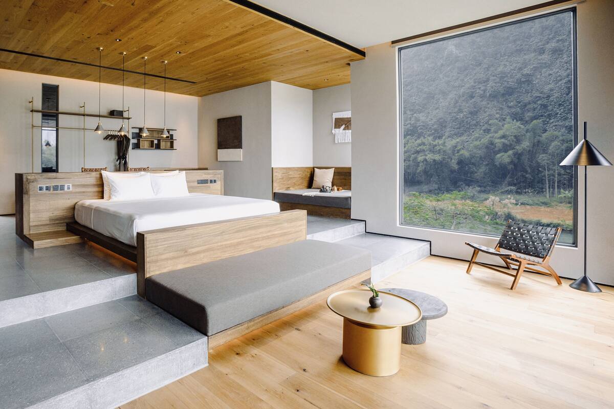 Un dormitorio moderno con una cama grande, una zona de estar y vistas a un bosque a través de un ventanal.