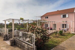 A pink house with a tiled roof, a white fence, and a garden with a pergola.