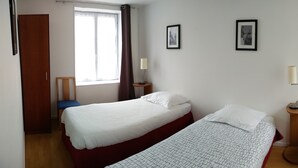 A bedroom with two beds, a window, a door, and two framed pictures on the wall.