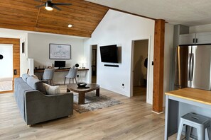 Un salon moderne avec un canapé gris, une table basse en bois et un téléviseur à écran plat fixé au mur.