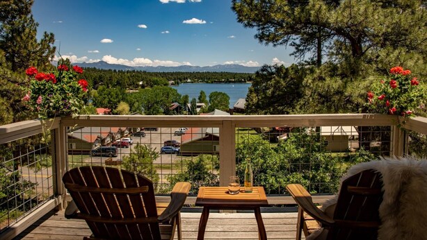 Een houten terras met twee stoelen en een tafel, met uitzicht op een meer en bergen.