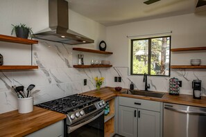 Une cuisine moderne avec un dosseret en marbre, des plans de travail en bois, des appareils en acier inoxydable et des étagères intégrées.