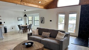 Een moderne woonkamer met een grijze bank, een houten salontafel, en een eethoek met een tafel en stoelen.