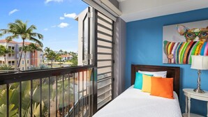 Un balcón con vistas a palmeras y edificios, una cama con almohadas de colores y un cuadro de un zorro en la pared.