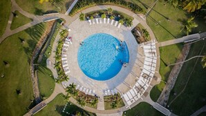 Vista aérea de una piscina circular rodeada de zonas de descanso y palmeras.