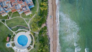 Vista aérea de un complejo turístico con piscina central, playa y zona residencial con edificios.