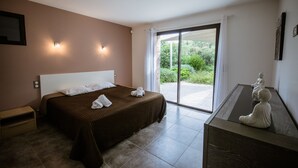 A bedroom with a large bed, a nightstand, a desk with a statue, and a sliding glass door leading to a garden. - Modern villa with private pool and garden, in a secure estate (Porto-Vecchio)