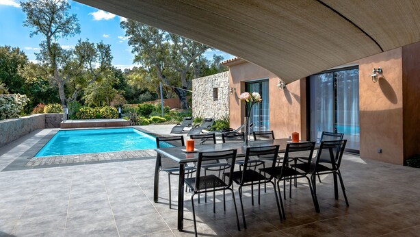 A poolside area with a table and chairs, a stone wall, and a view of trees and a building. - Modern villa with private pool and garden, in a secure estate (Porto-Vecchio)