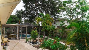 Ein überdachter Patio-Bereich mit Pool, Gartenmöbeln und verschiedenen Pflanzen.