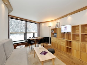 A cozy living room with a sofa, a dining table, and a TV on a wooden cabinet.