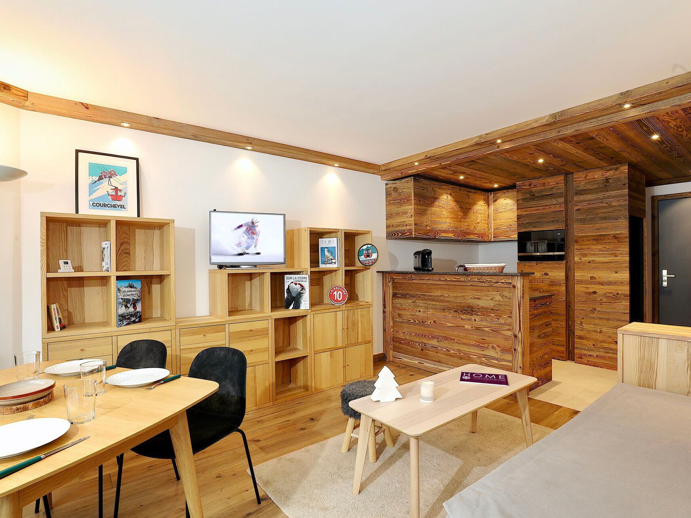 A cozy room with a wooden dining table, chairs, a TV, and a kitchen area with wooden cabinets.